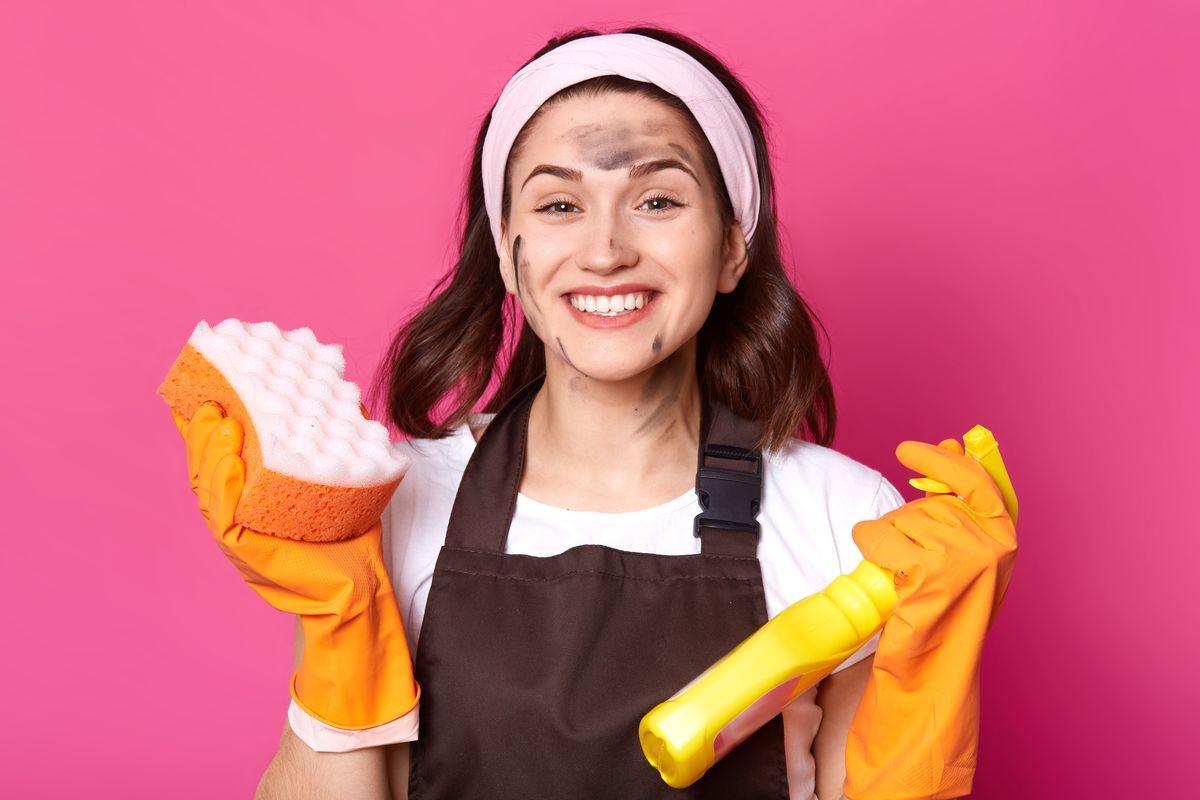 Cheerful energetic bright young woman looks happy isolated over pink background in studio, ready to do general cleaning, stain her face while tiding up, wearing working clothes. Household concept.